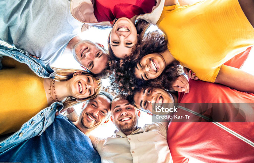 Multiracial group of young people standing in circle and smiling at camera - Happy diverse friends having fun hugging together - Low angle view